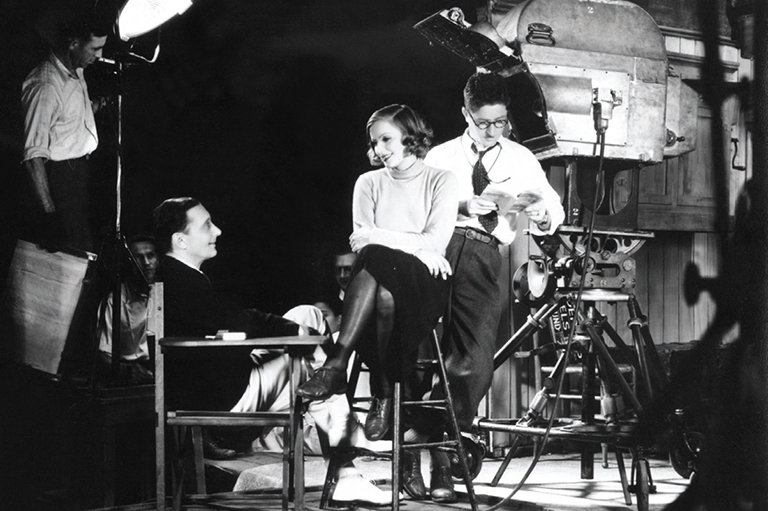 large camera and a man and woman face each other on a film set. 