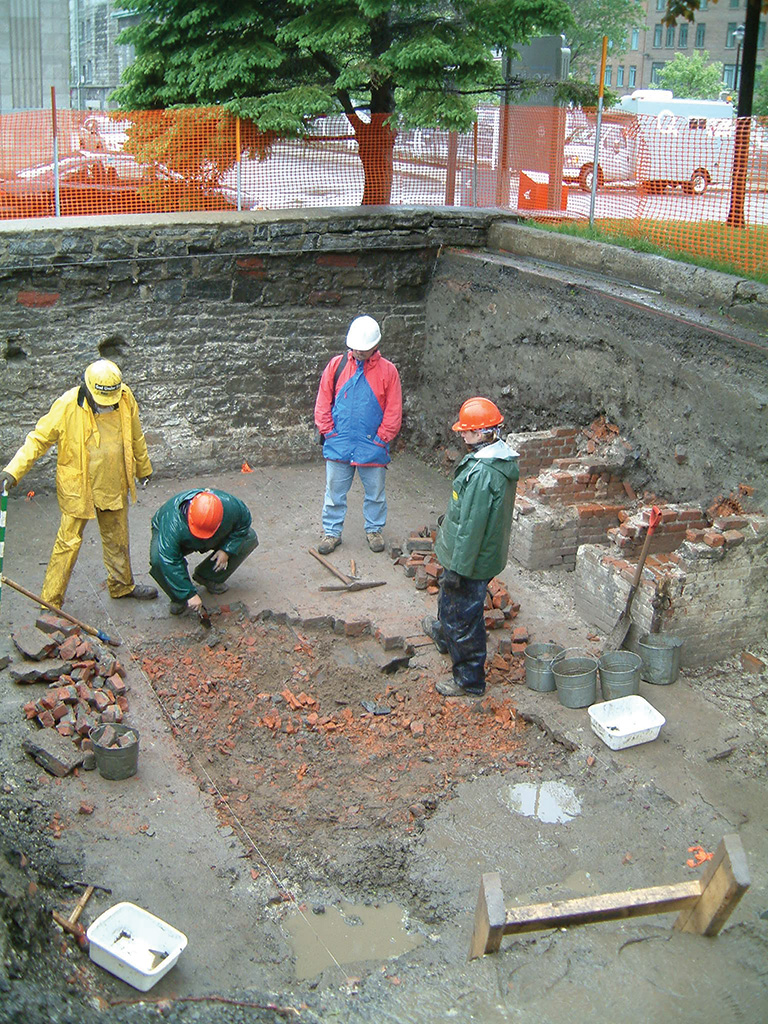 People wearing hard hats standing in an archaeological site looking at the ground 