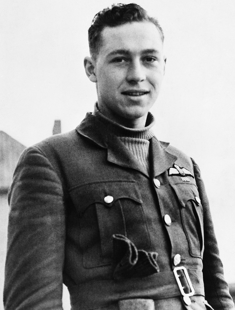This image shows a young man looking into the camera with a half smile. He is wearing a turtleneck and a blazer. 