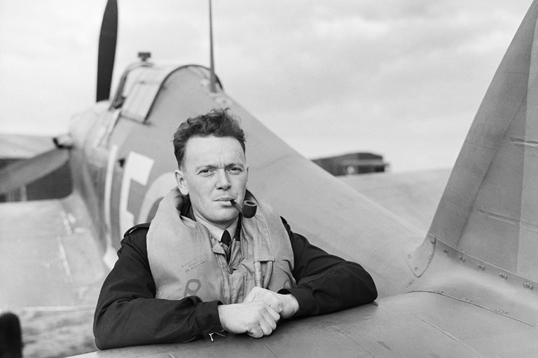 This image shows a man leaning forward on an airplane wing with a tobacco pipe in his mouth.