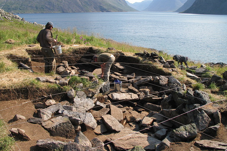 An coastal archaeological site with rocks and ropes and people working.
