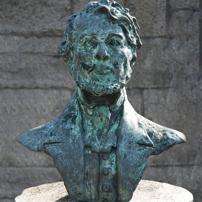 A metal bust sits in front of a stone wall.