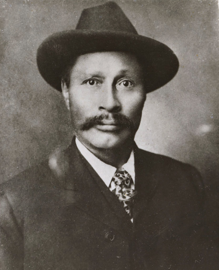 Black and white portrait of a man with a moustache wearing a short brimmed hat.