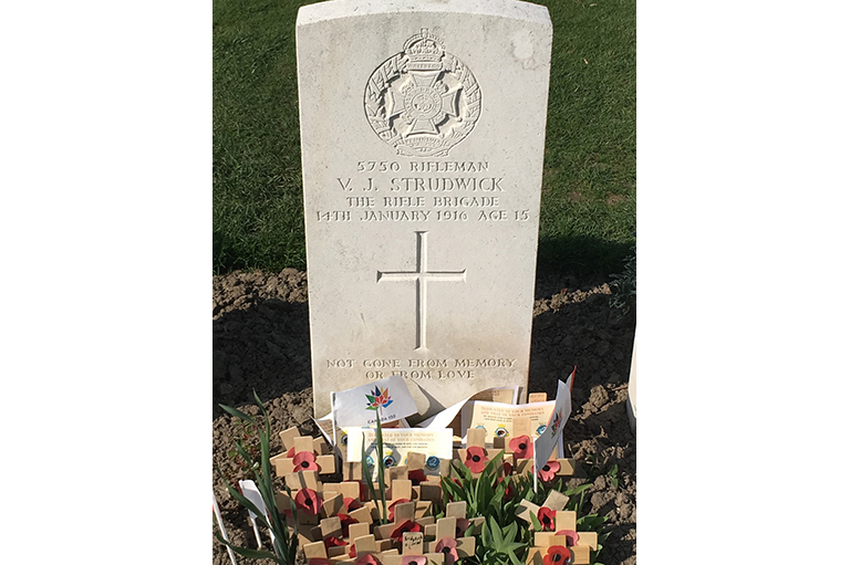 Image of a head stone with handmade crosses and poppy in front. 