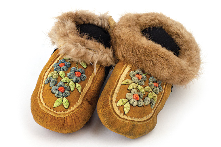 Brown animal skin moccasins with blue flowers on the front and fur trim around the ankles.