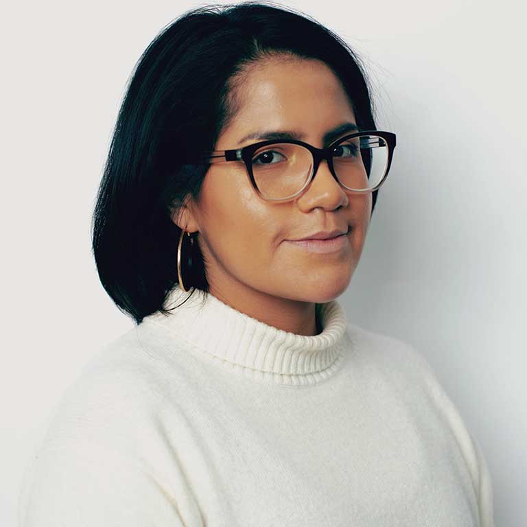 Portrait of a woman with black hair and glasses wearing a white turtleneck.
