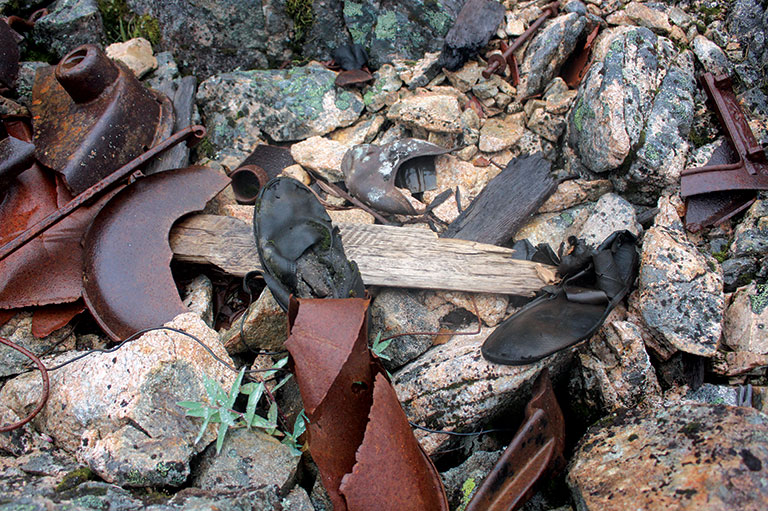 Black shoes and pieces of rusted metal are strewn amongst some rocks.