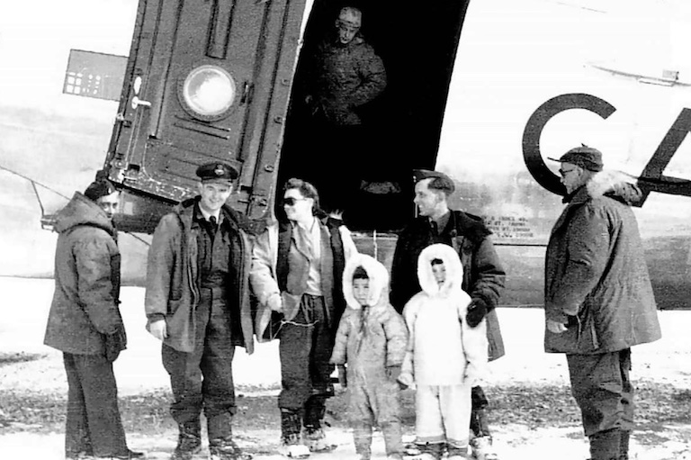Black and white photo of four adults standing around the entrance to a plane with two Inuit children.