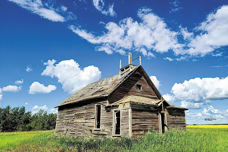 An abandoned farmhouse on green grass against a bright blue sky.