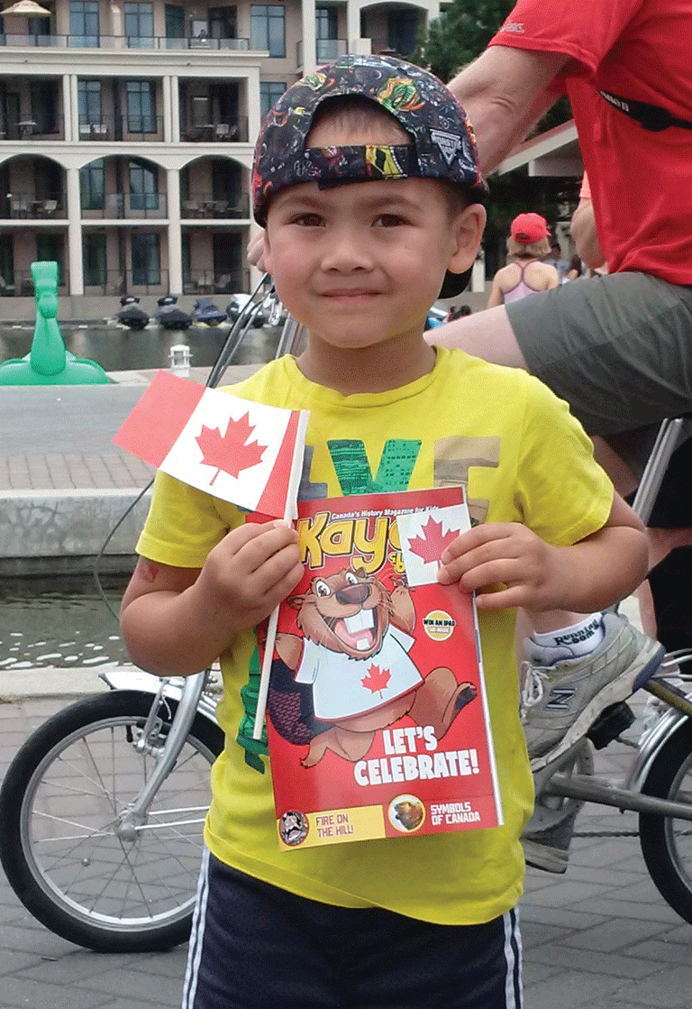 Young boy holds <em>Kayak: Canada's History for Kids</em> magazine and Canada flag. 