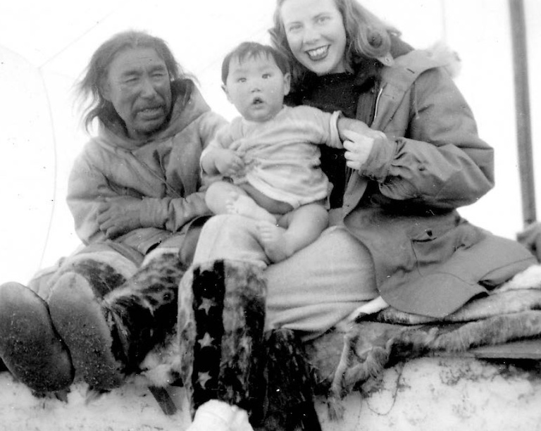Black and white photo of a white woman holding an Inuit child sitting beside and Inuit man.