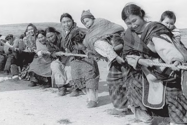 A group of people hold a rope and smile while playing tug of war.