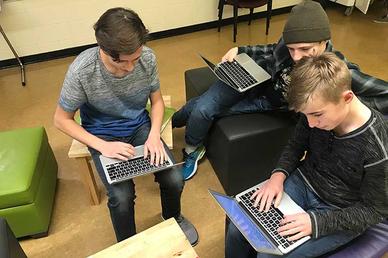 This image shows three male grade nine students on their computers in a casual learning space. 