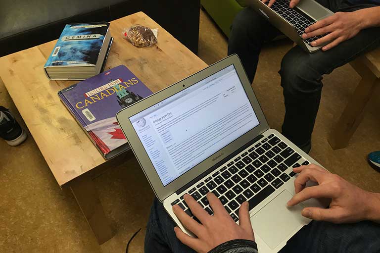 In this image there is a computer with hands at the keyboard. The screen is showing the Orange Shirt Day Wikipedia article. 