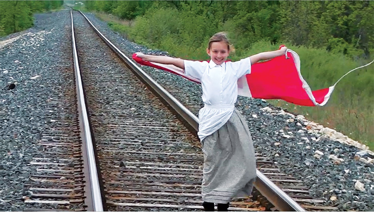 Photo from a scene of a video showing a Young Citizen on train tracks holding a flag.