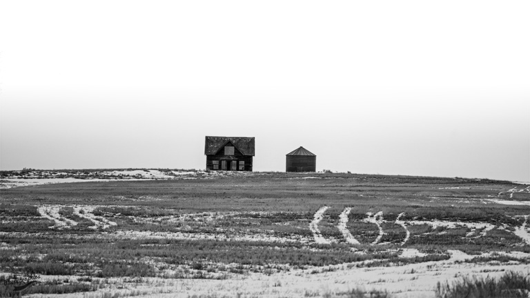 Black and white photo of a house and silo from a distance.