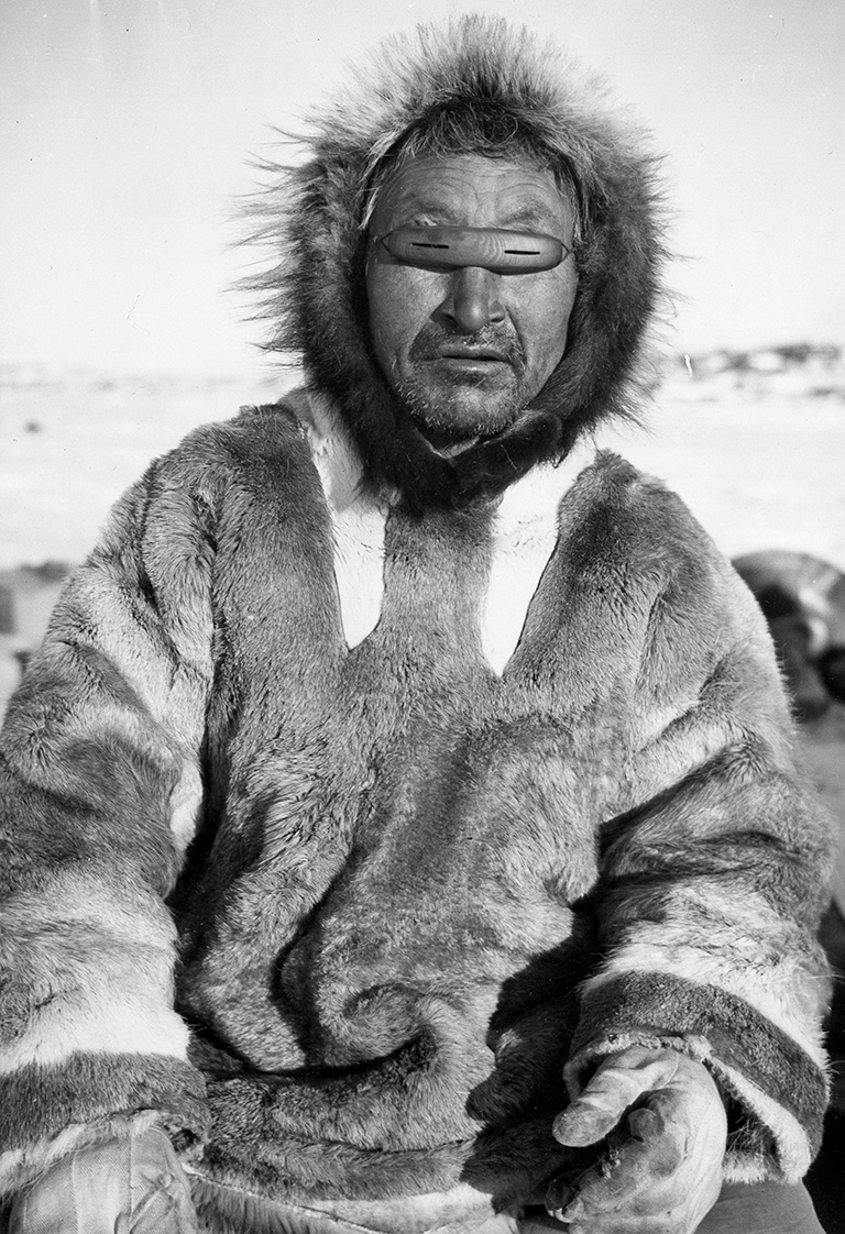 Black and white photo of a man in a parka with wood goggles with thin slits in them.