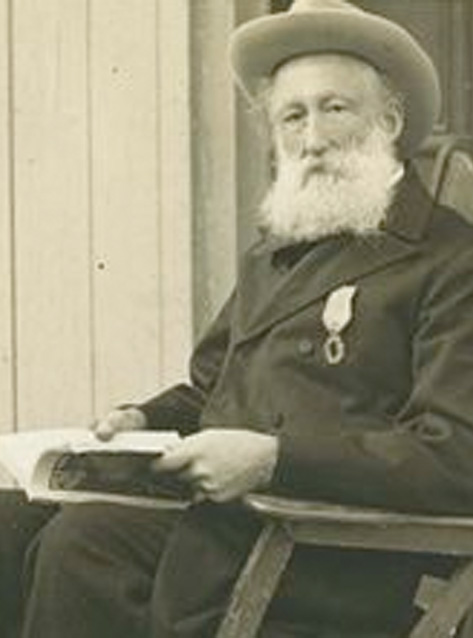 A man with a white beard sits with a hat on his head