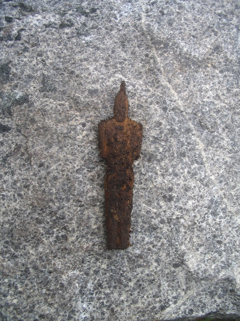 An eroding wooden doll with a rock as the background.