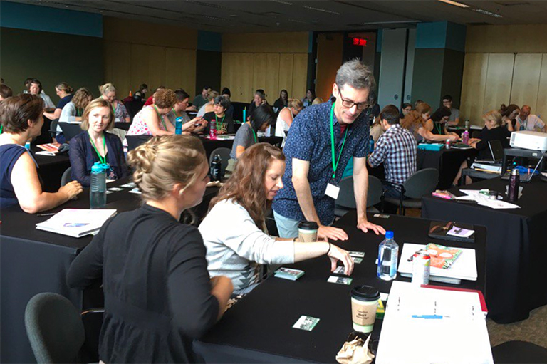 This image shows rows of tables with different people sitting in chairs all engaged in conversation at their tables. 