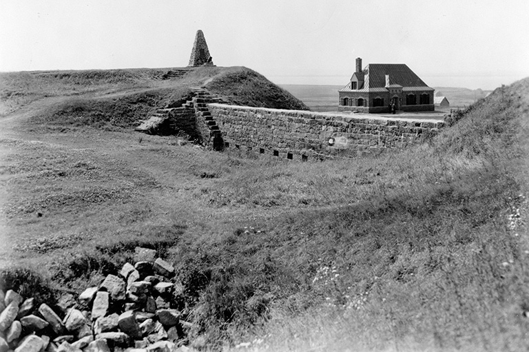 A grassy field with a stone wall and a house in the background. 