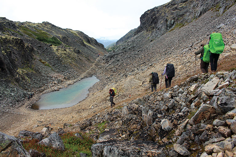 A photo shows hikers walking along a rocky path with large rocks in the background.