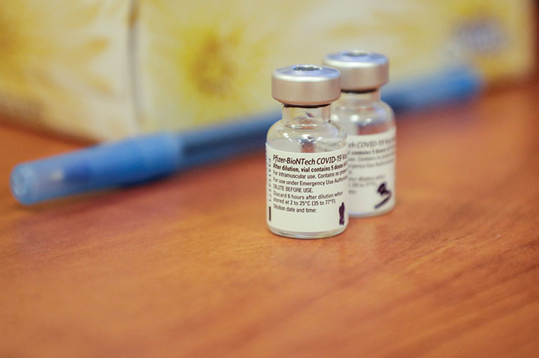 A close-up of two vials of Pfizer vaccine sitting on a table.