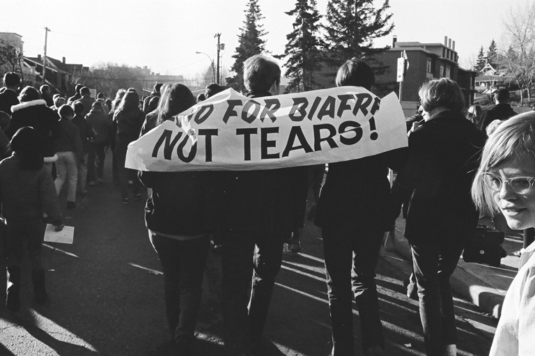 A group of people walking away from the camera holding a sign on their shoulders. 