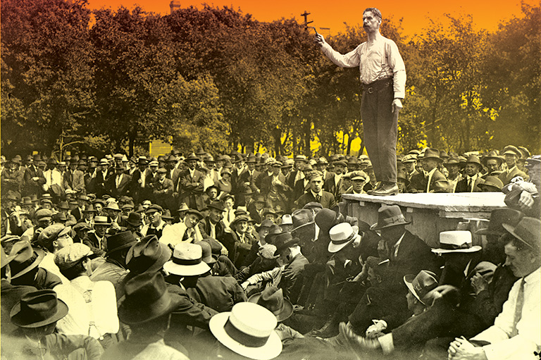 A colourized black-and-white image of many men in hats standing around listening to another man wearing suspenders standing on a box. 