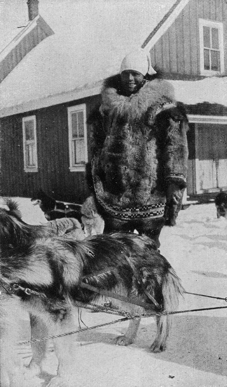 Black and white full body photo of a man standing outside wearing winter gear including a fur coat.