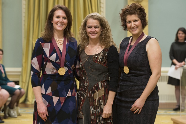 Two teachers wearing medals pose with the Governor General (centre)