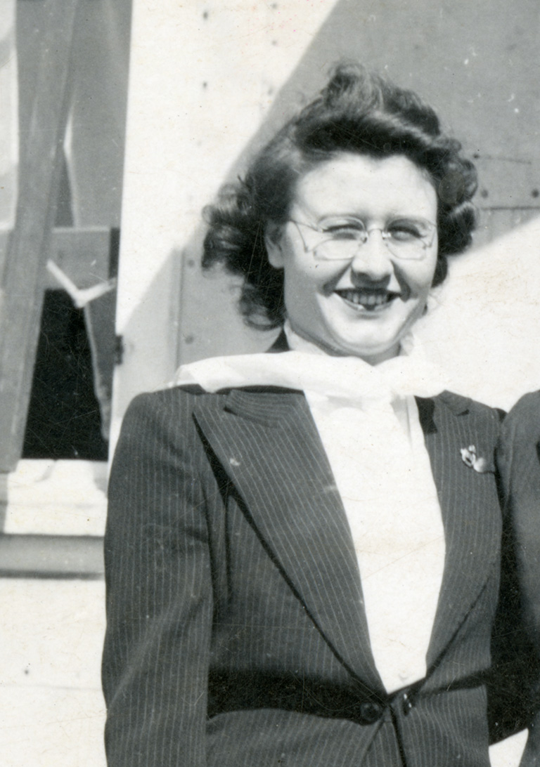 Black and white photo of a woman with glasses and brown hair. She smiles as the wind blows a scarf around her neck.