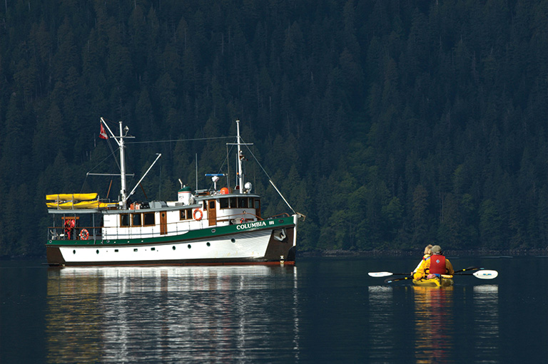 a large boat and a kayak in water in front of a forest. 