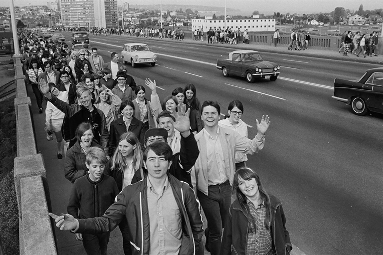 A crowd of people walk along a busy road 