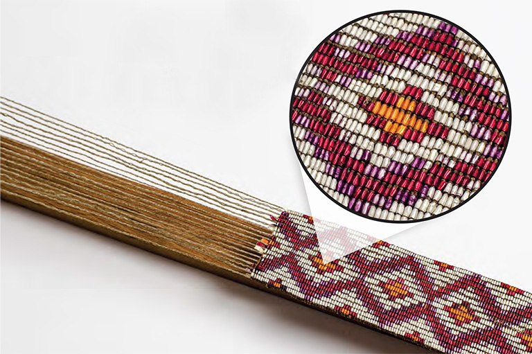 A photo of an artifact shows a close-up on some patterned weaving towards the base of the object.