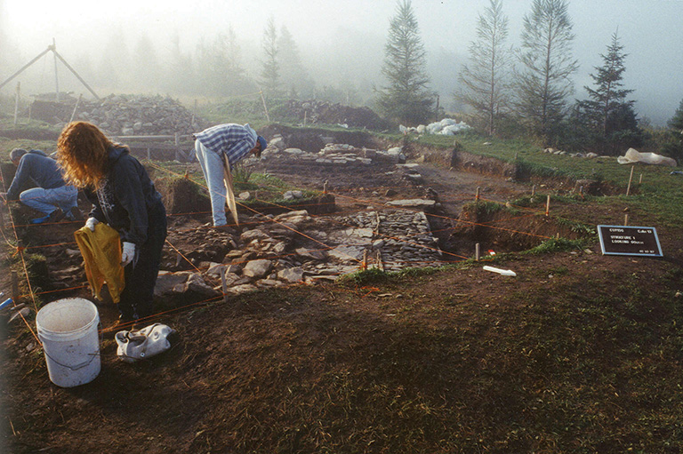 Excavation site with people bent over carrying buckets in the fog. 