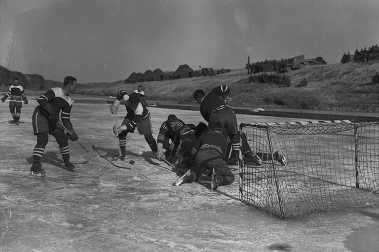 This image shows men playing hockey on a frozen river in front of a net. 